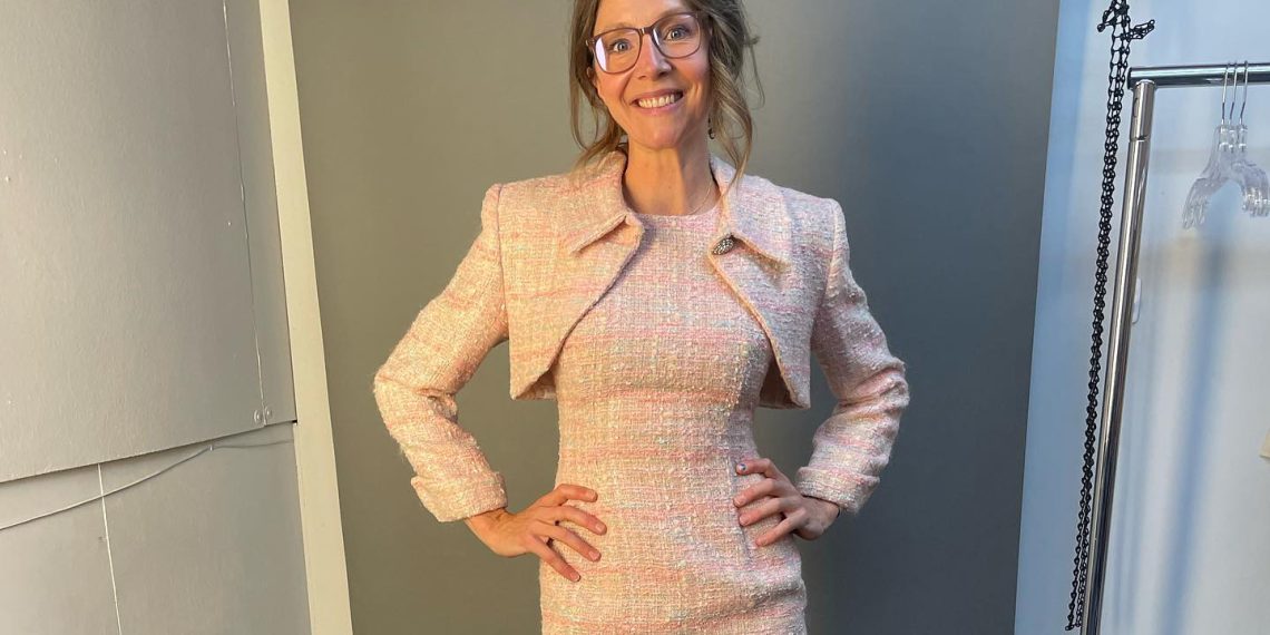 Sarah posing in a cream colored outfit and wearing glasses.
