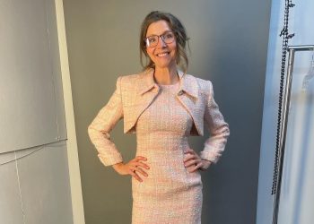 Sarah posing in a cream colored outfit and wearing glasses.