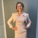 Sarah posing in a cream colored outfit and wearing glasses.
